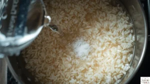 Pouring water into a saucepan with toasted rice and garlic to begin cooking the arroz blanco.