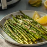 Crispy air fryer asparagus recipe-served on a white plate with lemon wedges and a sprinkle of Parmesan cheese, fresh and golden-tipped.