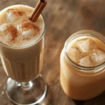 Glass of authentic horchata recipe with ice cubes, cinnamon powder dust, and cinnamon stick, next to a jar filled with horchata on a rustic wooden table.