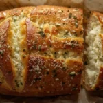 Golden Italian herb and cheese bread loaf topped with melted mozzarella and parmesan, sliced to show its soft, fluffy inside.