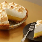 How to make lemon meringue pie – whole pie with one slice served on a plate with fork, golden meringue and creamy lemon filling.